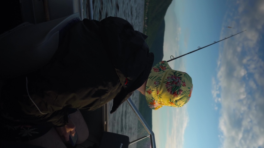 A man is sailing on a boat with a fishing rod in his hands. A fisherman holds a rod with bait while swimming to a fishing spot. View from the back.