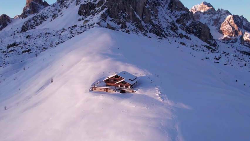 Mountain lodge in winter snow in front of Ra Gusela mountain peak, sunset, aerial Royalty-Free Stock Footage #1093379729