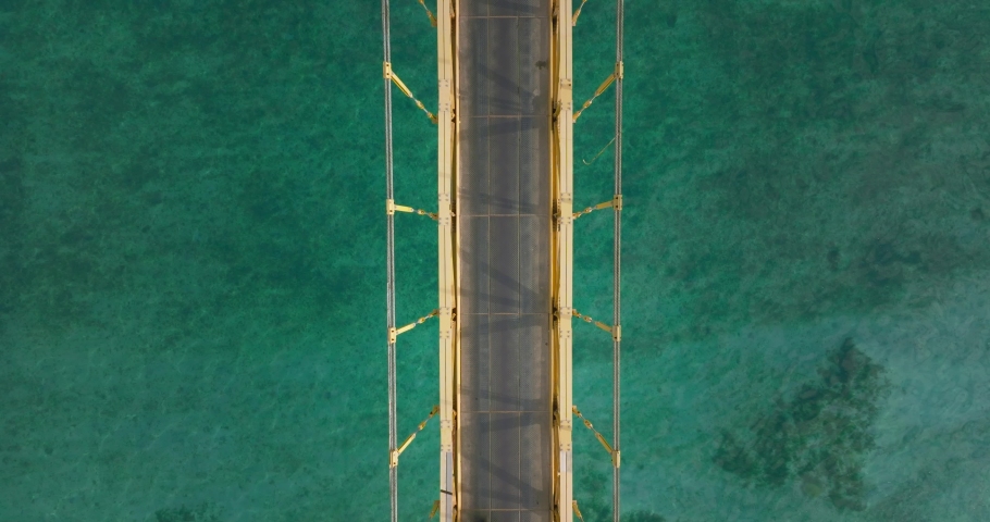 Scooters crossing on yellow bridge with turquoise water below, stationary top down