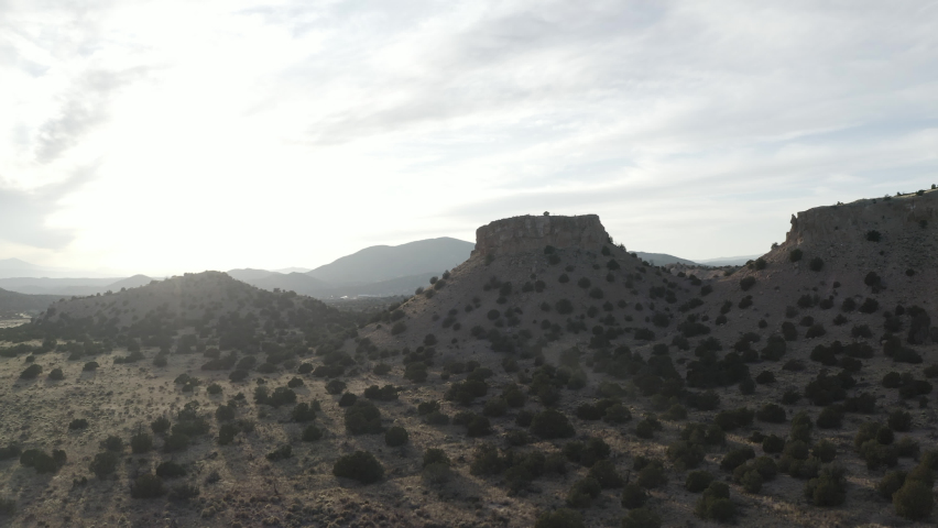 Drone shot circles a rock formation in the desert as sunset shines through brush