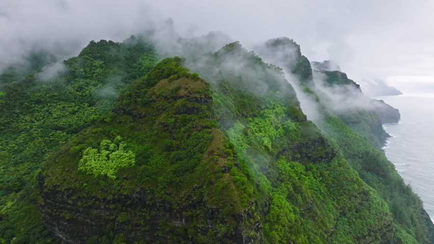 Flying through rain clouds above green mountain tops covered by tropical jungle rainforest. High peaks at Na Pali coast park, wonderful rainy summer day natural landscape.Epic Hawaii island