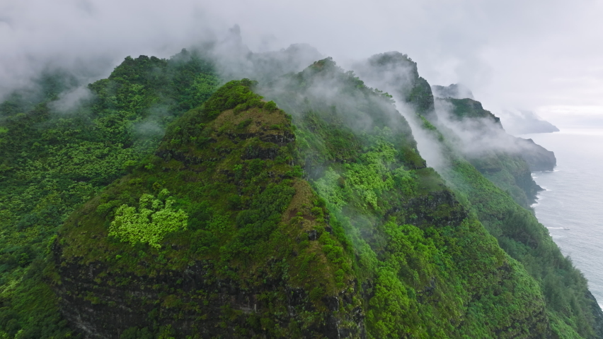 Flying through rain clouds above green mountain tops covered by tropical jungle rainforest. High peaks at Na Pali coast park, wonderful rainy summer day natural landscape.Epic Hawaii island Royalty-Free Stock Footage #1093389295