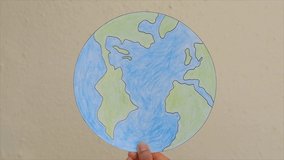 Crayon drawing of the Earth held up by a hand against a plain wall. Clip for educational videos on planet conservation and sustainability or even on Global Warming and Climate Change.