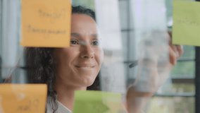 Close-up young pensive businesswoman project organizer writing down new tasks on sticky colored notes developing idea puts reminder creates strategy plans workflow attaching stickers on glass board - Powered by Shutterstock - Get 15% off with code: PIKWIZARD15