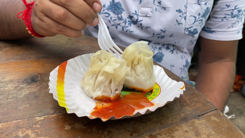 Man eating delicious cooked Momo filled with succulent chicken mince in TIRETTA BAZAR, Kolkata, using a plastic fork.