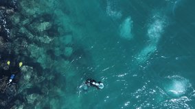 High view of scuba divers exploring a rocky shoreline with bubbles breaking the ocean surface. Drone video