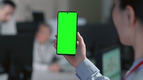 Close up of woman holding smartphone with green screen. Female employee use mobile phone at work in modern office