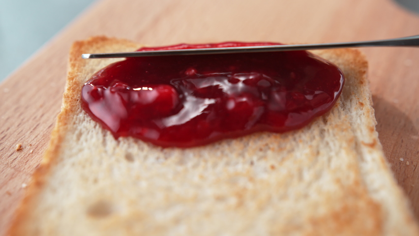 Spreading Red Jam on a Slightly Browned Toast with Table Knife on Cutting Board in Slow Motion - Dolly Out Royalty-Free Stock Footage #1093404921