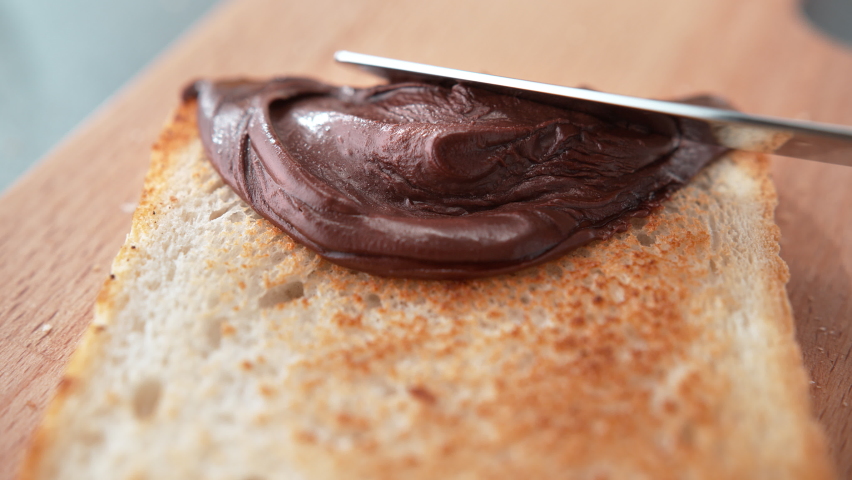 Spreading Chocolate Spread on a Slightly Browned Toast with Butter Knife on Cutting Board in Slow Motion Royalty-Free Stock Footage #1093404925