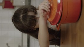 The little girl waits at the table for the meal prepared by her mother. When the girl lifts the lid of the pot, she is very happy to see that her mother is cooking her favorite dish.Vertical video.