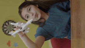 Bored schoolgirl playing with her toys at a table in her home. A 10-12 year old child is playing with a small model airplane, she is doing it. Portrait of a student.Vertical video. - Powered by Shutterstock - Get 15% off with code: PIKWIZARD15