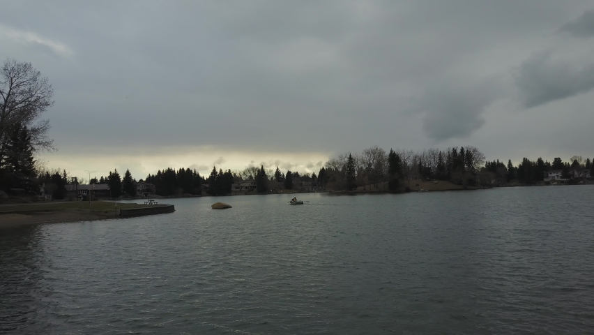 Man is rowing in a small boat on a lake with sunset shining through stormy clouds
