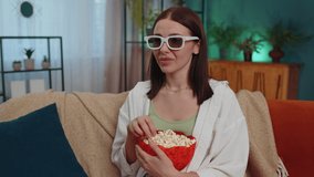 Excited adult girl sitting on sofa eating popcorn and watching interesting tv serial, sport game, film, online social media movie content online at home. Young woman enjoying domestic entertainment