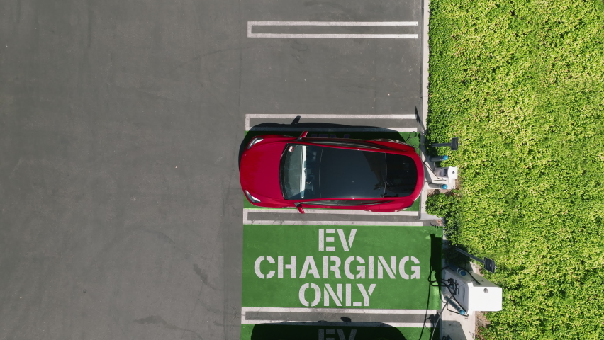 Aerial view of red car charging in green business park. 4K electric, zero pollution cars on green energy concept on modern city parking lot. Alternative energy for ecological cars, zoom in drone 4K Royalty-Free Stock Footage #1093423969