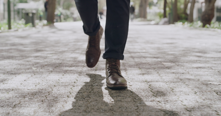 Feet of a fashionable business man walking, taking steps forward in a city. Male wearing formal shoes, enjoying a relaxed stroll in a park. Guy having a peaceful walk in a street