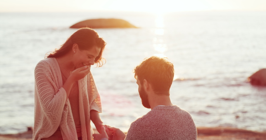Romantic, romance and engagement proposal at the beach by boyfriend to surprise his girlfriend with a ring. Happy, in love and young man asking to marry a woman at sea on a summer evening sunset | Shutterstock HD Video #1093431203