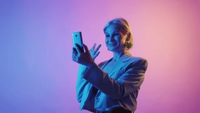 Video call. Modern senior. Mobile communication. Joyful stylish mature woman talking on phone online chat in multicolor neon light.