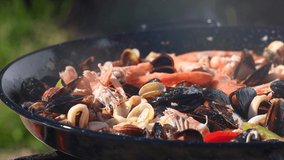 Paella traditional Spanish food, seafood paella in the fry pan with mussels, king prawns, langoustine and squids. Person cooking paella outside. Slow motion 4K UHD video