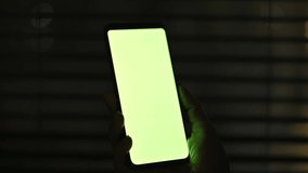Close-up of female hands hold smartphone with mock up green screen chroma key at night. Girl watching video, online conference, film, browsing social networks, news, surfing Internet, online