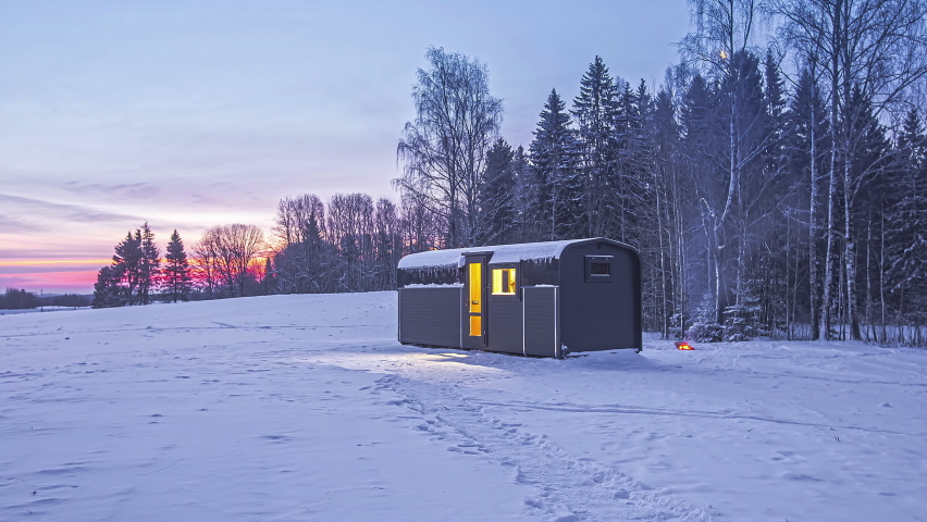 Timelapse shot of people walking around a wooden cabin surrounded by cold winter landscape at dawn.