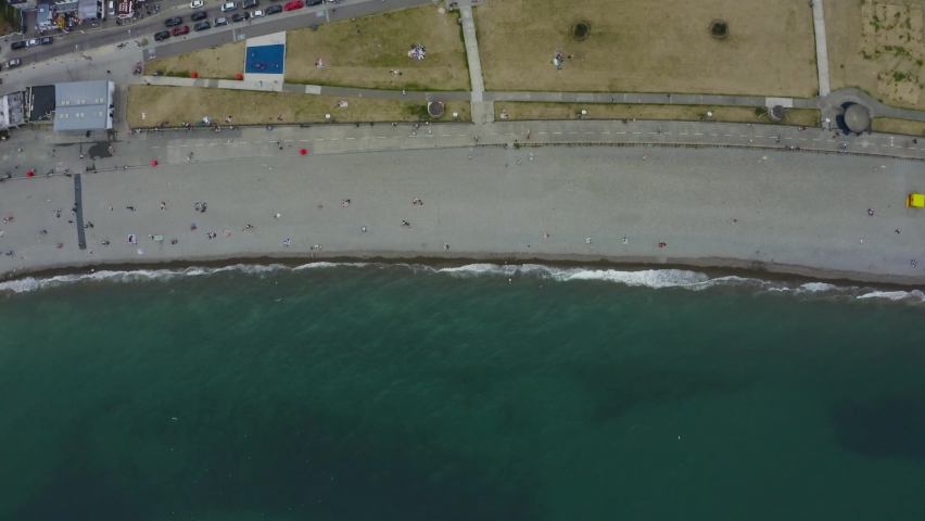 Aerial top-down view of Bray Town with busy streets, parking lots full of cars and many people at the beach. Travel and tourism concept