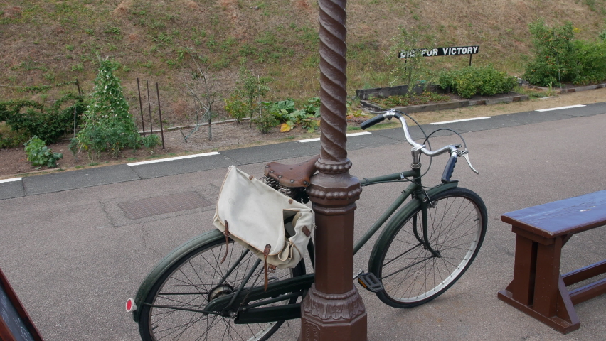 A vintage bicycle leaning on a post at a train station during world war two with a British dig for victory sign