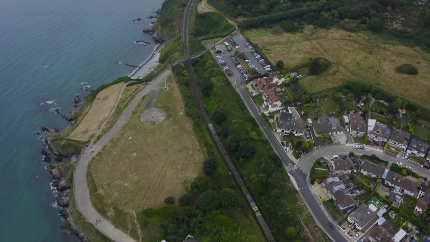 Aerial top-down shot of the passenger train going towards Greystones Train Station along the cliffs by the sea. Bray, County Wicklow, Ireland. Travel and Tourism concept