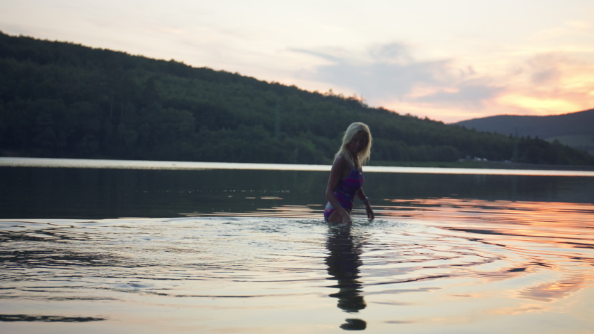 Rear view of active senior woman swimmer diving outdoors in lake.