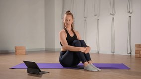 Determined athletic woman exercising, stretching exercises on yoga mat while watching online fitness course video on tablet. Woman practicing yoga online with laptop