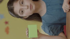 Girl holding green box on table in nursery, showing a product, smiling and presenting an imaginary object. Creative 3d artists can replace the green box with any product they want.Vertical video.