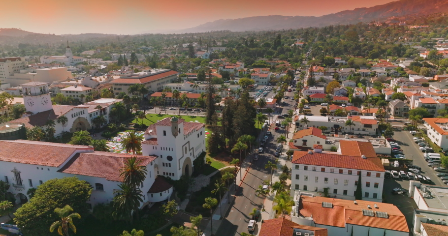 Lovely white houses with orange roofs, numerous cars on the streets and parking lots. Beautiful architecture and hills of Santa Barbara at backdrop of pink skies. Royalty-Free Stock Footage #1093451185