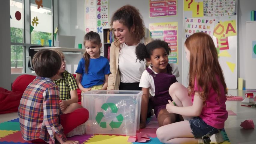 Teacher giving recycle lesson to little kids in kindergarten. Protect nature, save environment. Diverse preschool children learn to sort garbage in primary school putting plastic bottles in recycle | Shutterstock HD Video #1093459655