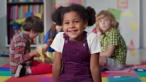 Close up portrait of smiling little African-American girl looking at camera at primary school. Adorable preschool kid sitting in playroom of kindergarten - Powered by Shutterstock - Get 15% off with code: PIKWIZARD15