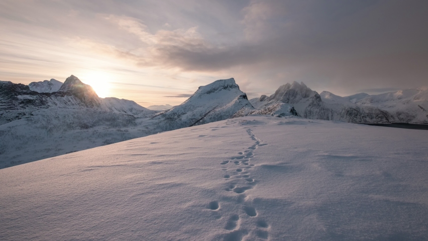 Time lapse of Sunrise over snowy mountain peak with footprint on winter in the morning at Segla mount, Senja island, Norway