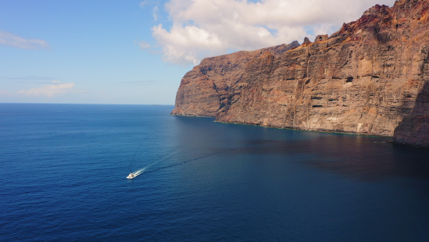 High flight and top view of huge rocky mountains. Los Gigantes cliffs. White boat is sailing on ocean. Aerial. Holiday mood, willingness to travel again. Go everywhere. Tenerife, Canary islands. | Shutterstock HD Video #1093468769