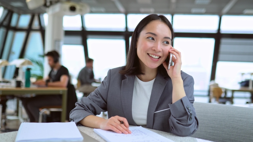 Young Chinese business woman talking on phone working in modern office. Asian businesswoman hr manager wearing suit making call on cellphone having mobile job interview sitting at work in office. | Shutterstock HD Video #1093471439