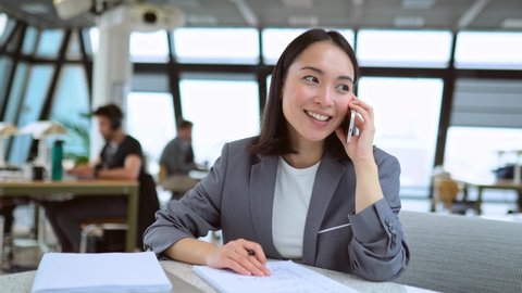 Young Chinese business woman talking on phone working in modern office. Asian businesswoman hr manager wearing suit making call on cellphone having mobile job interview sitting at work in office. 庫存影片