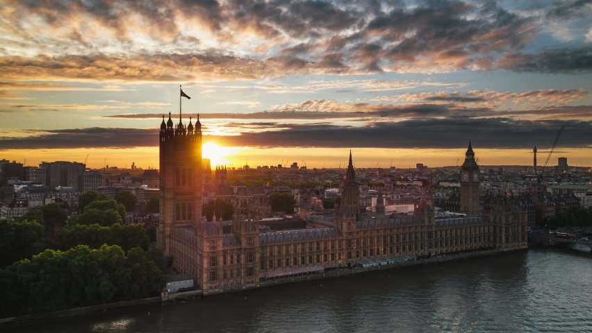 Establishing Aerial View Shot of London UK, United Kingdom, Westminster, sun peaks from behind Elizabeth Tower, magical sunset over parliament, Big Ben