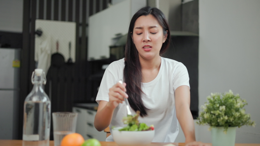 Unhappy female looking to organic greens vegetable salad in weight loss diet and wellness on table. Tired woman dislike eat bored with food healthy salad breakfast in kitchen. Diet food concept. Royalty-Free Stock Footage #1093493367