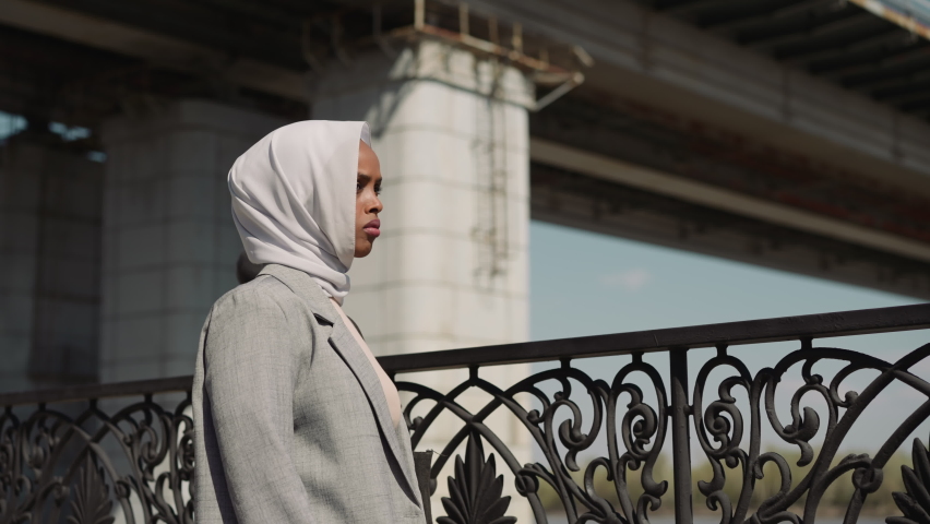 Sad Arabian woman with white hijab stands by fence on embankment close view. African-American lady against city overpass bridge. Urban architecture | Shutterstock HD Video #1093493853