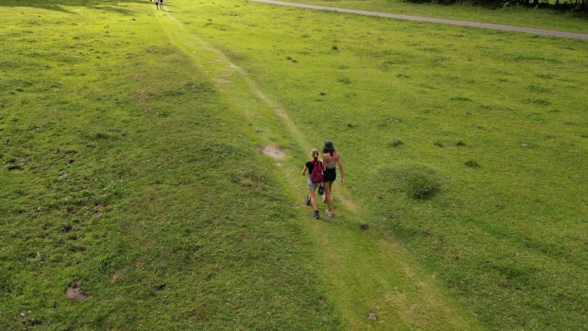 Two girls talk and walk on a small gravel path on a green meadow in the swiss alps, Obwalden, drone alp view