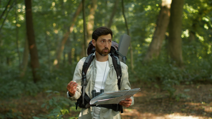 Orienteering in forest. Active man tourist with backpack got lost during hiking trip in woodland, looking for right way with compass and paper map, searching north, slow motion, free space Royalty-Free Stock Footage #1093497261