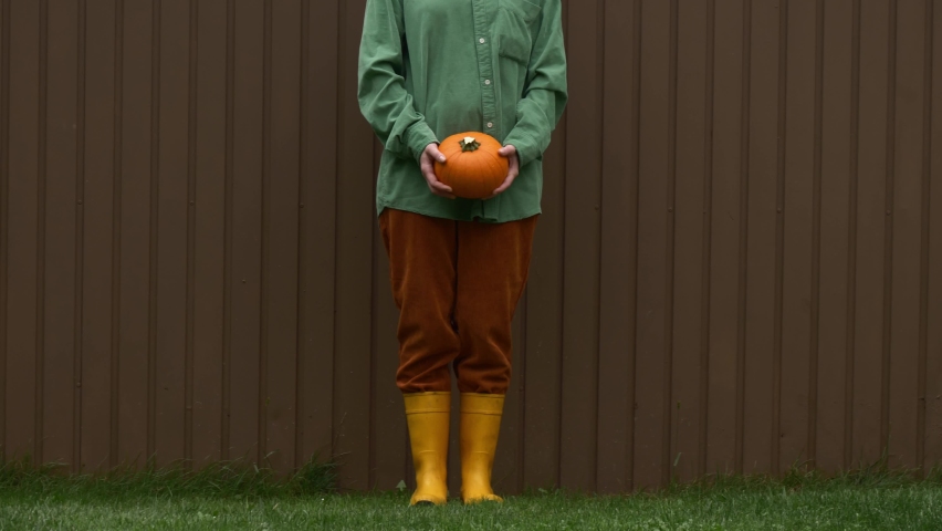 Stylish girl in green shirt, brown pants and yellow boots with pumpkin in a garden