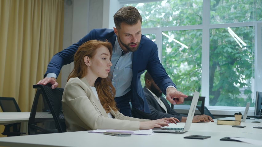 Man team leader brainstorming with businesswoman colleague using laptop computer showing ideas pointing at computer screen working together in office