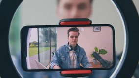 Male vlogger wearing headphones live streaming podcast looking on mobile phone - shot in slow motion