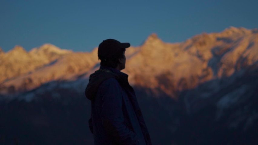 Silhouette shot of an Indian man staring at the snow covered mountains during the sunset at Manali in Himachal Pradesh, India. Man staring at the beautiful mountain peaks during sunset. | Shutterstock HD Video #1093521907