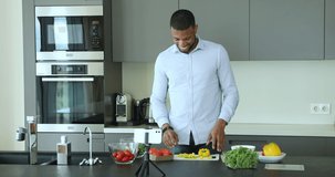African man, chef cooking in fashionable kitchen record cook class use smartphone camera. Food blogger make stream preparing vegetarian salad at modern home. Tech, vlogging activity, cookery concept