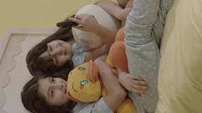 Two little sisters watching an exciting movie wrapped in their plush toys. Siblings watching tv in bed. Entertainment, Emotions, Children Watching TV, Watch Cartoons.Vertical video.