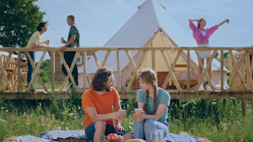 Romantic couple in love spending time at campsite while sitting on the haystack feeling great together other people enjoy the time at nature beside them at campsite