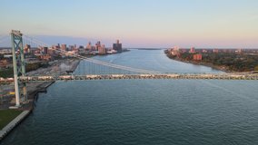 Aerial drone footage of the Ambassador Bridge crossing over the Detroit River during a beautiful summer sunset. Semi trucks crossing the bridge and a Lake Freighter passing underneath the bridge.